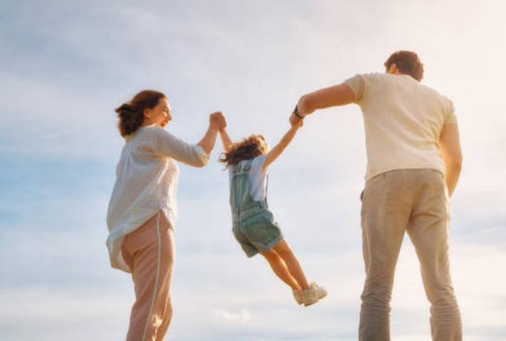 Foto von Mutter und Vater von hinten die ein Kind durch die Luft schaukeln